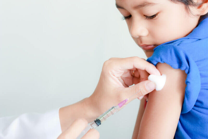 Young child in blue shirt receiving a vaccine injection in the arm from a healthcare professional