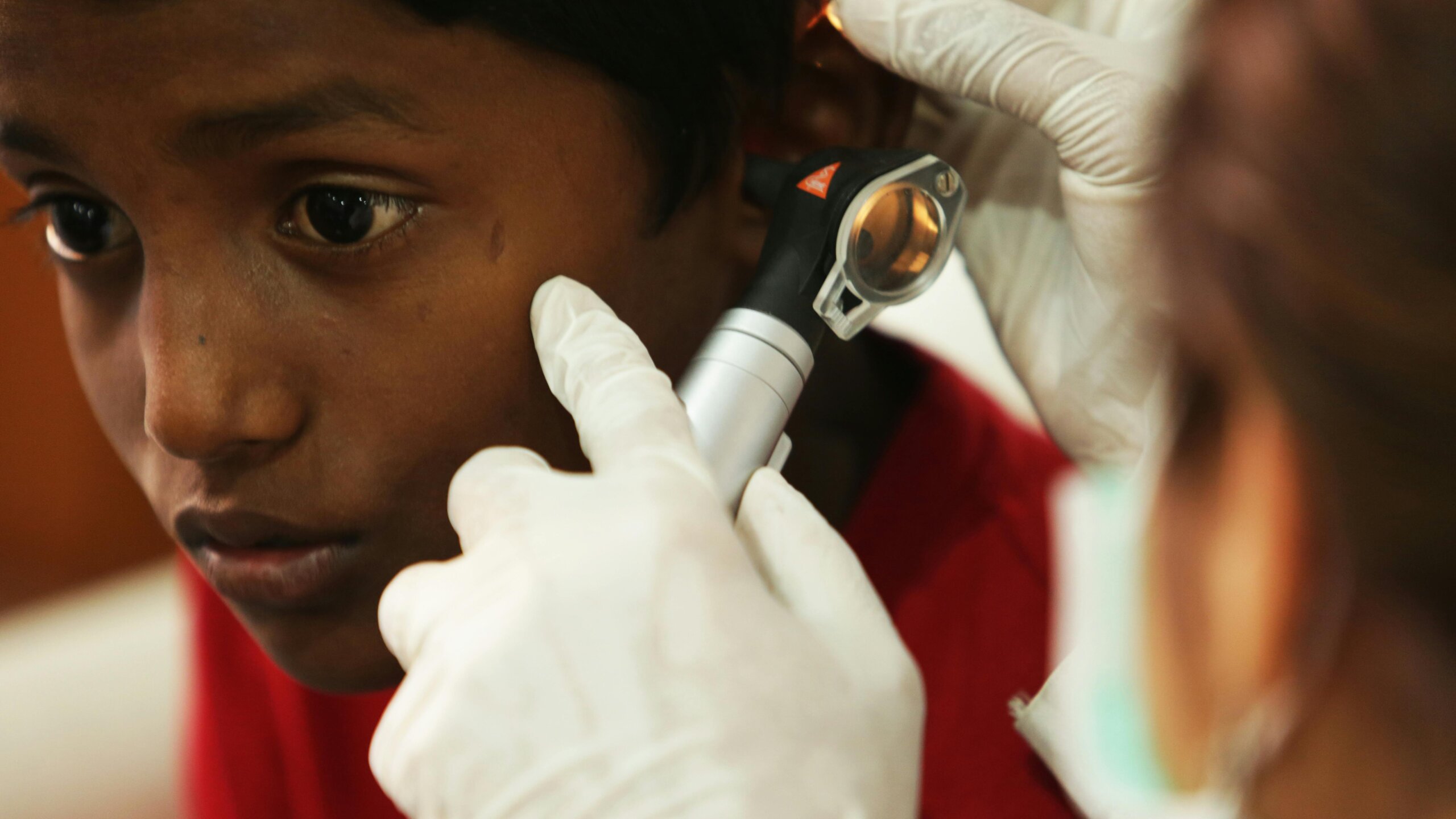 Close-up of a healthcare worker examining a child’s ear with an otoscope during a medical check-up.